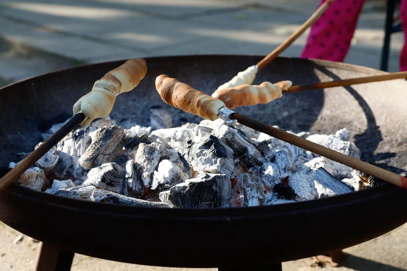 Es ist eine Feuerschale mit Glut und 4 Stäben zu sehen, an den Stockbrot gemacht wird.